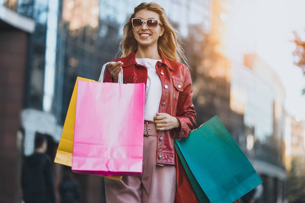 Γυναίκα το περπάτημα στο δρόμο εκμετάλλευση σακούλες για ψώνια. Αγοραστής χαμογελά ευτυχισμένη περπατώντας στο δρόμο μετά από ψώνια - Φωτογραφία, εικόνα