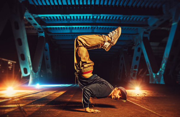 Young cool man break dancer standing on hands upside down. Urban bridge with cool and warm lights background. - Foto, Imagem