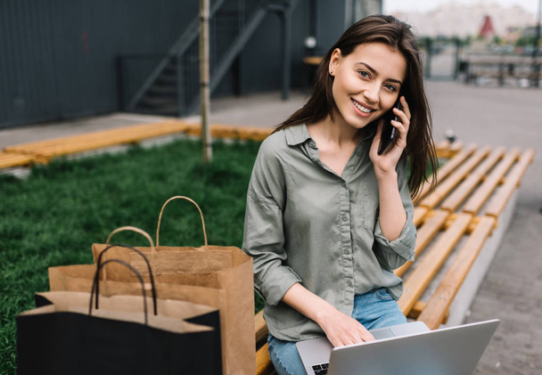 Cheerful happy business woman with beautiful smile wearing stylish clothes using laptop computer and mobile phone for online shopping. Freelancer working online - Фото, зображення