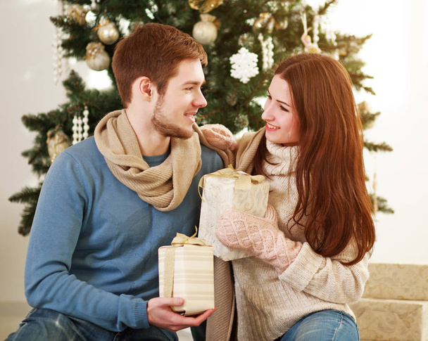 Молодая семейная пара влюбленных дома на Рождество на фоне новогодней елки дарить подарки
 - Фото, изображение