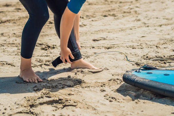 Woman fastening leash across legs with surf for beginner on sandy beach. - Photo, Image