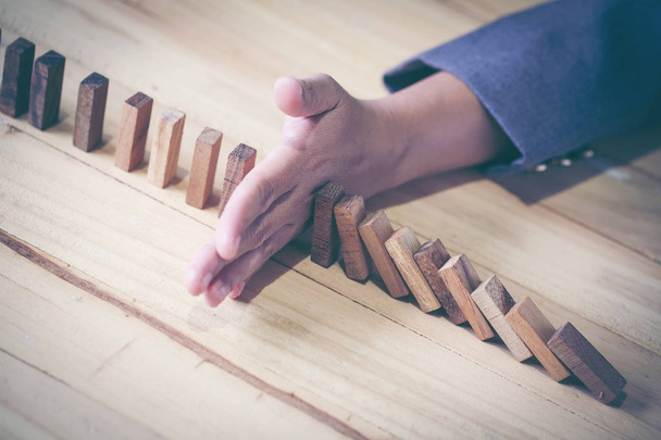Woman stopping domino effect on wooden table. Business success concept. Copy space. - Photo, Image