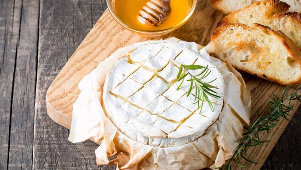 Baked camembert cheese. Fresh Brie cheese and a slice on a wooden board with nuts, honey, rosemary, baguette bread grilled toasts and leaves. Brie type of cheese. Italian, French cheese. - Zdjęcie, obraz