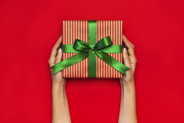 Geschenkkarton mit grünem Band in Frauenhand auf rotem Hintergrund von oben flach liegend. Urlaubskonzept Neujahr oder Weihnachten Geschenk-Box Geschenke Weihnachten Urlaub Glückwünsche Hintergrund mit Platz für Text - Foto, Bild