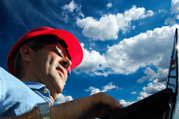 Közelről mérnök használ laptop szabadban ragyogó kék ég háttér alacsony szögből készült portréja - Fotó, kép