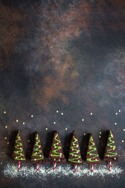 Chocolate Brownies in shape of Christmas Trees with green icing and festive sprinkles, top view, copy space. Sweet Christmas or winter holidays pastry food concept. - Fotoğraf, Görsel