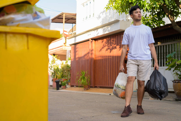 Genç Asyalı adam çöpü dışarı çıkarıyor.  - Fotoğraf, Görsel