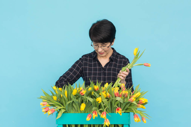 Очаровательная флористка сортирует тюльпаны в коробке, выбирает их для будущей цветочной композиции.
. - Фото, изображение