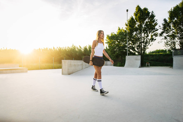 Stylish young woman skating outdoors - Pretty female skater playing with her skate - Foto, imagen