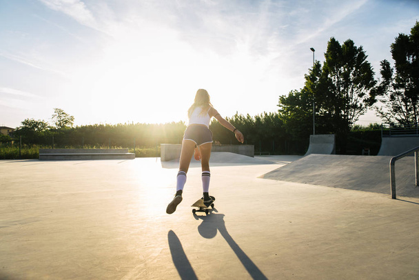 Stylish young woman skating outdoors - Pretty female skater playing with her skate - Foto, Bild