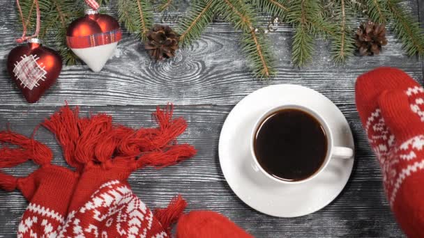 Kellemes karácsonyi ünnepeket és boldog új évet 2019 2020 fogalom. Piros kötött ujjatlan kezét vesz egy csésze forró kávét, egy fából készült háttér ki ahol újév szimbólumok kerülnek. Fenyő fa ágai, karácsonyi játékok - Felvétel, videó