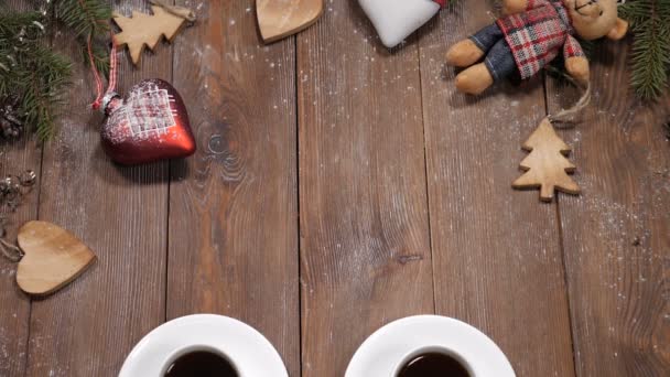 Merry Christmas and happy new year concept. Cups of coffee placed on wooden background together with fir tree branches and heartshaped toys. Merry christmas note is put near cups - Footage, Video