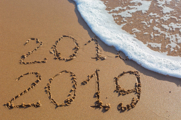 2018 2019 merkintä kirjoitettu märkä keltainen ranta hiekka pestään merivesiaallolla. Ajatus juhlia uutta vuotta jossain eksoottisessa paikassa
. - Valokuva, kuva