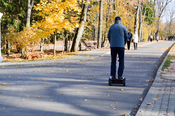 Een man rijdt in de herfst park op een tweewielige hoverboard. Uitzicht vanaf de achterkant - Foto, afbeelding