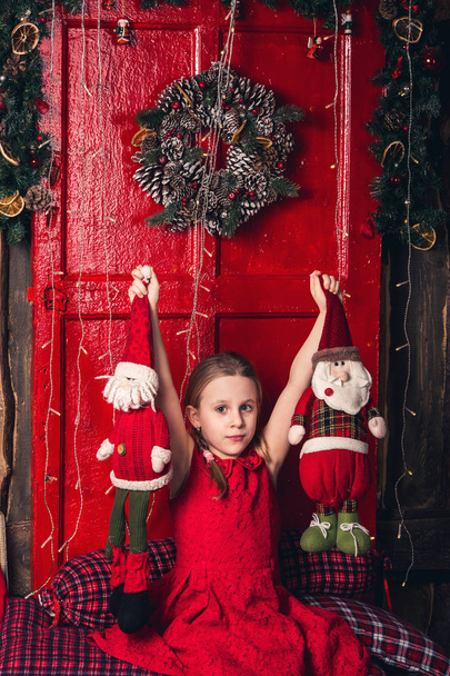 A girl in a red dress holds toy Santa and an elf in her hands. - Photo, Image