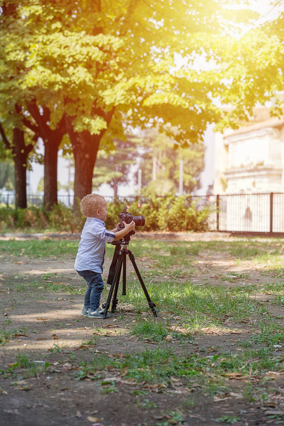 Little boy photographing on the camera on tripod in the park - 写真・画像
