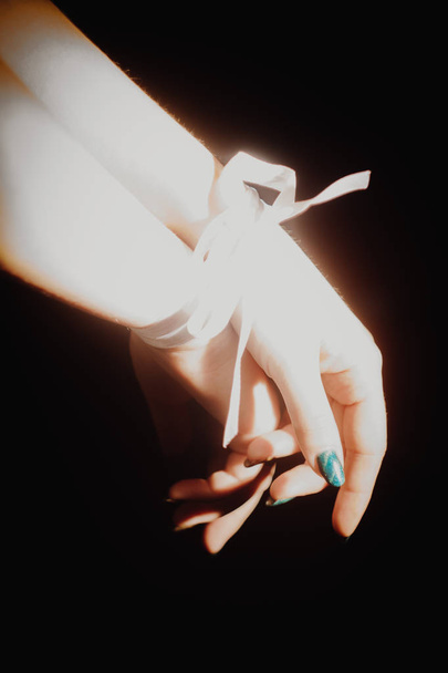 tied hands with ribbon isolated on black background highlighted with light - Foto, immagini