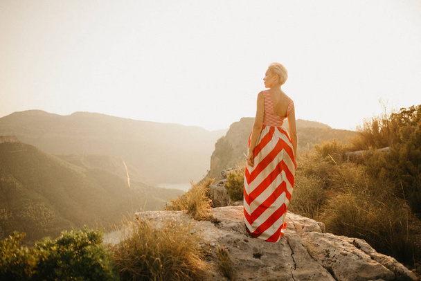オレンジ色の夕日に川と古代峡谷の背中でポーズ赤いドレスでブロンドの女の子。スペイン - 写真・画像