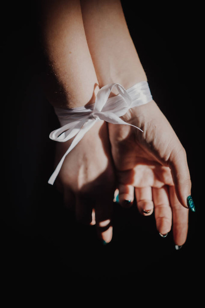 tied hands with ribbon isolated on black background highlighted with light - Foto, Imagen