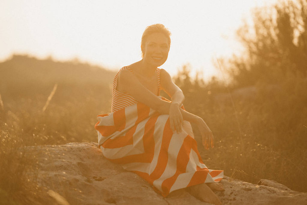 Una graziosa giovane donna attraente con le braccia incrociate posa sulla grande pietra nell'antico canyon alla luce del sole arancione. Spagna
 - Foto, immagini