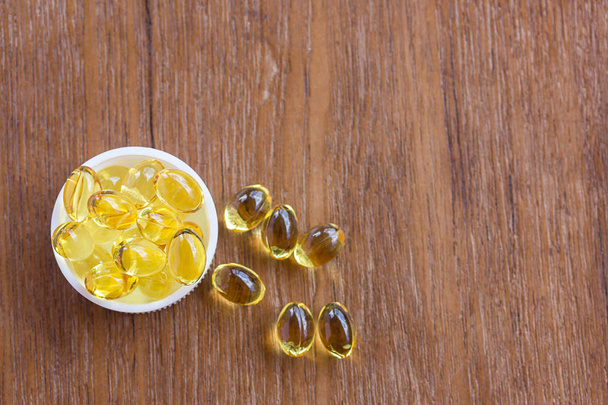Fish oil pouring out from bottle of medicine. Cod liver oil omega 3 gel capsules on wooden background - Photo, Image