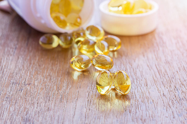 Omega 3 vis-lever olie capsules in houten achtergrond. Stapel grote gouden doorschijnend pillen in kleine glazen kom. Gezond dagelijks vetzuren voeding aanvullen. Bovenaanzicht plat lag met kopie ruimte - Foto, afbeelding