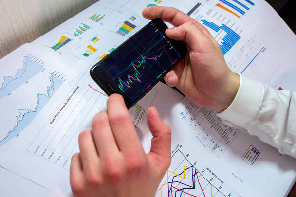man's hand touching phone screen with graphics on background of financial documents.  - Foto, Bild