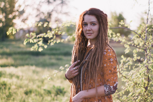 Portrait of beautiful hippie woman with dreadlocks in the woods at sunset having good time outdoors - Photo, image