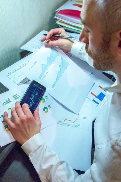 A businessman holding phone and pen on background of financial documents. Concept of working place of businessman. - Valokuva, kuva