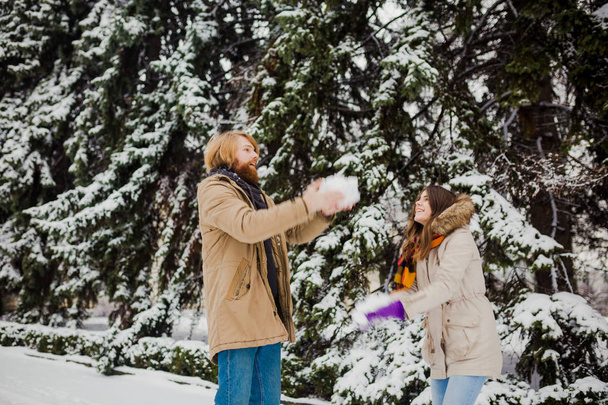 Kavkazské mladík s vousy a dívka mají venku v zimě parku na pozadí sněhové zasněžené jehličnatý strom play koule, hoďte sníh, datum oběsili a zimní hry. - Fotografie, Obrázek
