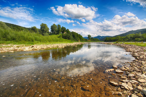 Mountain river stream of water in the rocks with blue sky and mirror reflection in water. Clear river with rocks leads towards mountains lit by sun. Carpathian region. Ukraine - Photo, Image