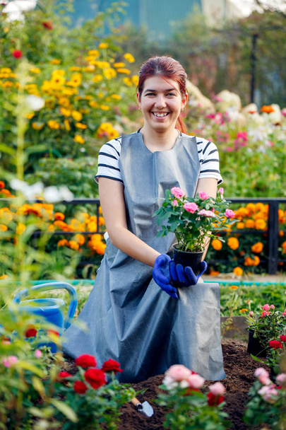 Image of smiling agronomist brunette holding pink roses in garden - Фото, изображение