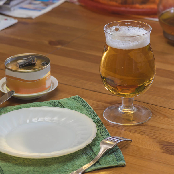 Склянка пива, тарілка, виделка і відкрита банка їжі на обідньому столі
 - Фото, зображення