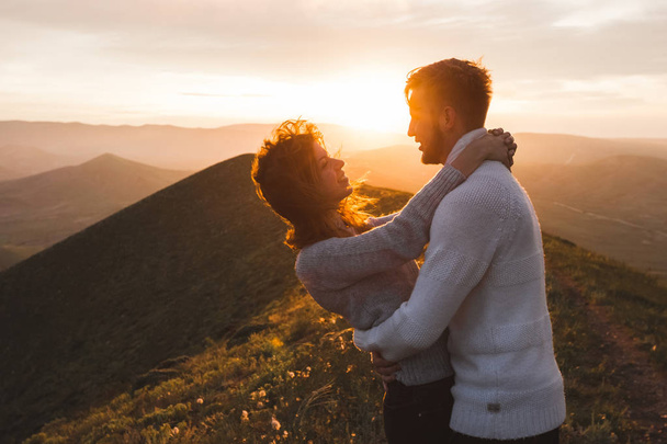 Счастливая пара обнимается и целуется на закате с удивительным видом на горы. Теплый вечерний солнечный свет
 - Фото, изображение