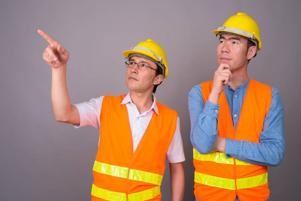 Two young Asian men construction worker together against gray ba - Photo, Image