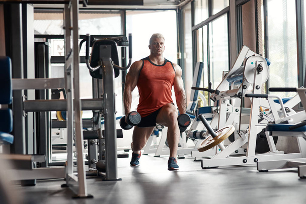 Bomba de hierro. Cintura para arriba de un hombre fuerte haciendo sentadillas con mancuernas en las manos mientras entrena en el gimnasio
 - Foto, imagen