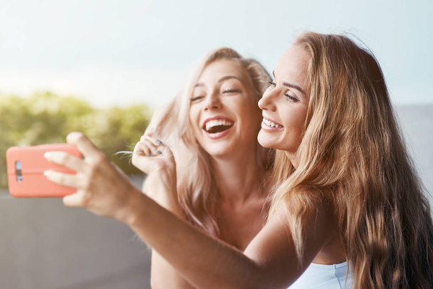 Δύο φίλες χρόνο μαζί με τα πόδια έξω στέκεται λήψη selfie φωτογραφίες για τα social media σε smartphone γελώντας χαρούμενη γκρο πλαν - Φωτογραφία, εικόνα