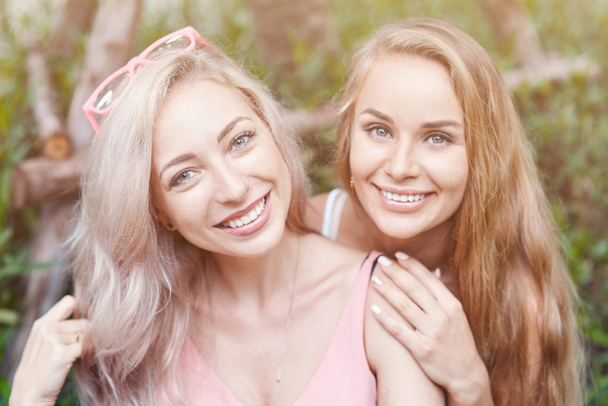 Two female friends time together standing in floral background hugging looking camera smiling happy - Photo, Image