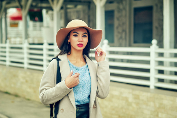 Retrato de una joven en las calles de la ciudad de otoño. Una chica con un sombrero de fieltro de ala ancha y un abrigo ligero
 - Foto, imagen