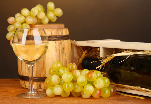 Wooden case with wine bottle, barrel, wineglass and grape on wooden table on brown background - Photo, Image