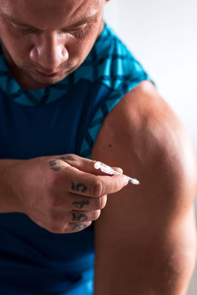 Amplify the strength. Close up of a professional strongman holding a syringe while injecting steroids - Zdjęcie, obraz