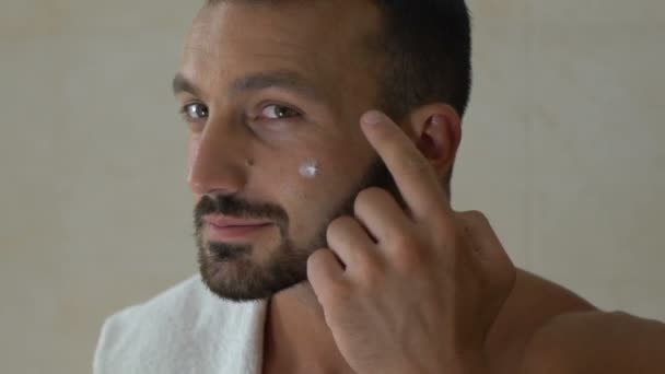 Man applying cream on his face in front of mirror in bathroom, cosmetics for men - Materiaali, video