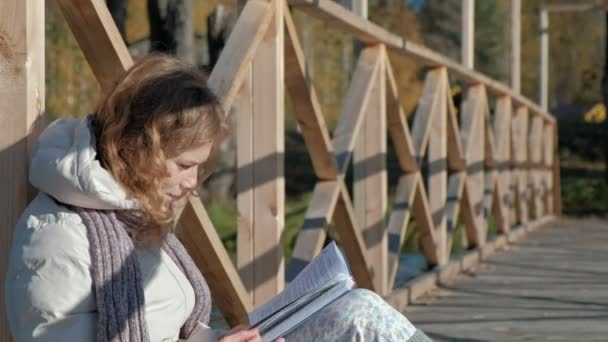 una mujer en el puente cerca del río de otoño lee un libro y bebe té
 - Imágenes, Vídeo