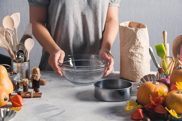 Woman cooking baking pack of flour pumpkins autumn time. Glass plate, sieve, pack of flour, physalis, kitchen tools, spices, leaves, gray background. - 写真・画像