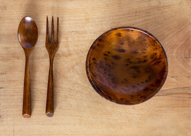 Wooden bowl, fork and spoon on a wooden background from above. Studio shot. Kitchen utensil. - Foto, Imagem