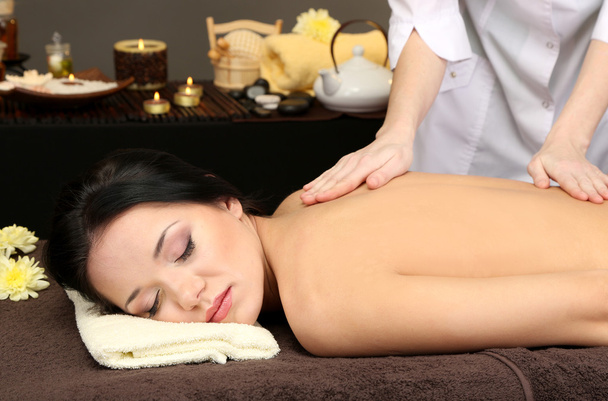 Beautiful young woman in spa salon getting massage, on dark background - Photo, Image