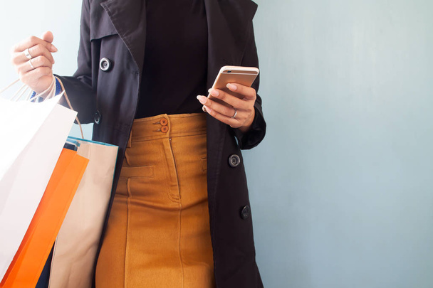Mujer con abrigo negro usando el teléfono móvil y bolsas de compras en la mano, concepto de compras
 - Foto, Imagen