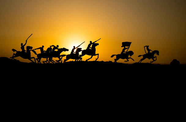 Attacking scene. War concept. Riders on horse ready to fight and soldiers on a dark foggy toned sunset background. Battle scene battlefield of fighting soldiers. Selective focus - Photo, Image