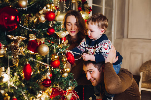 Onnelliset vanhemmat osoittavat joulukoristeen pienelle pojalle. - Valokuva, kuva