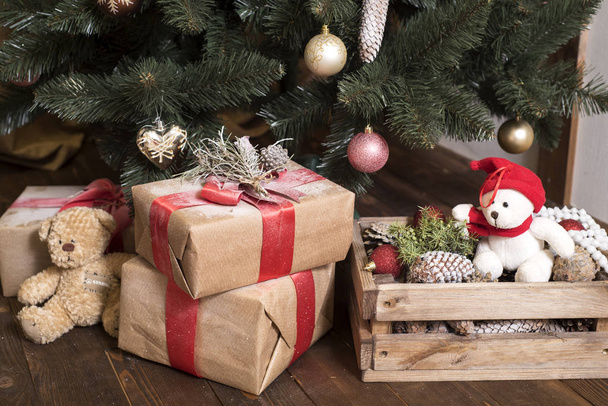 Bear wearing Santa hat with Christmas gift boxes on a white carpet at night. Many gifts in craft paper with a red ribbon under the tree. wooden box with snow. concept of merry christmas and new year - Photo, image
